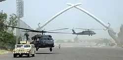 Dos helicópteros UH-60 Black Hawk tomando tierra frente a los sables del arco de la victoria en la Zona Internacional de Bagdad el 4 de julio de 2006.