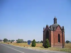 Photo of a small brick chapel on a highway amid rolling pastures. A sign reads Voghera to the right and Piacenza to the left.
