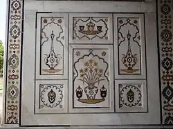 Floreros de pietra dura en el muro de mármol con bordura floral geométrica.