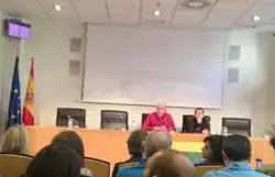 Ambos activistas están en una mesa hablando frente a las personas asistentes.