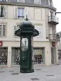 Una columna Morris en Épinal, con una fuente decorada con un mascarón en forma de cabeza de león.