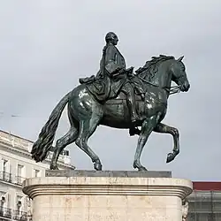 Estatua ecuestre de Carlos III, resultado de distintos proyectos (Manuel Francisco Álvarez de la Peña y Juan Pascual de Mena). Hay una estatua ecuestre anterior del mismo Carlos, como rey de Nápoles, por Antonio Canova, que comparte la Piazza del Plebiscito con otra de Fernando II, de Antonio Calì.[34]​