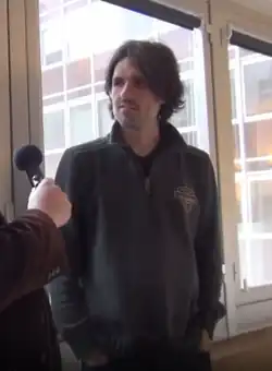 Hombre, manos en los bolsillos, con jersey oscuro.