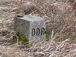 Square grey stone in scrubby brown grass with "DDR" carved on the right face.