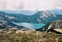 A mountain rising above a lake in the foreground with glaciated mountains in the background.