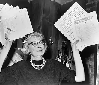 Woman in glasses waving documents in air.