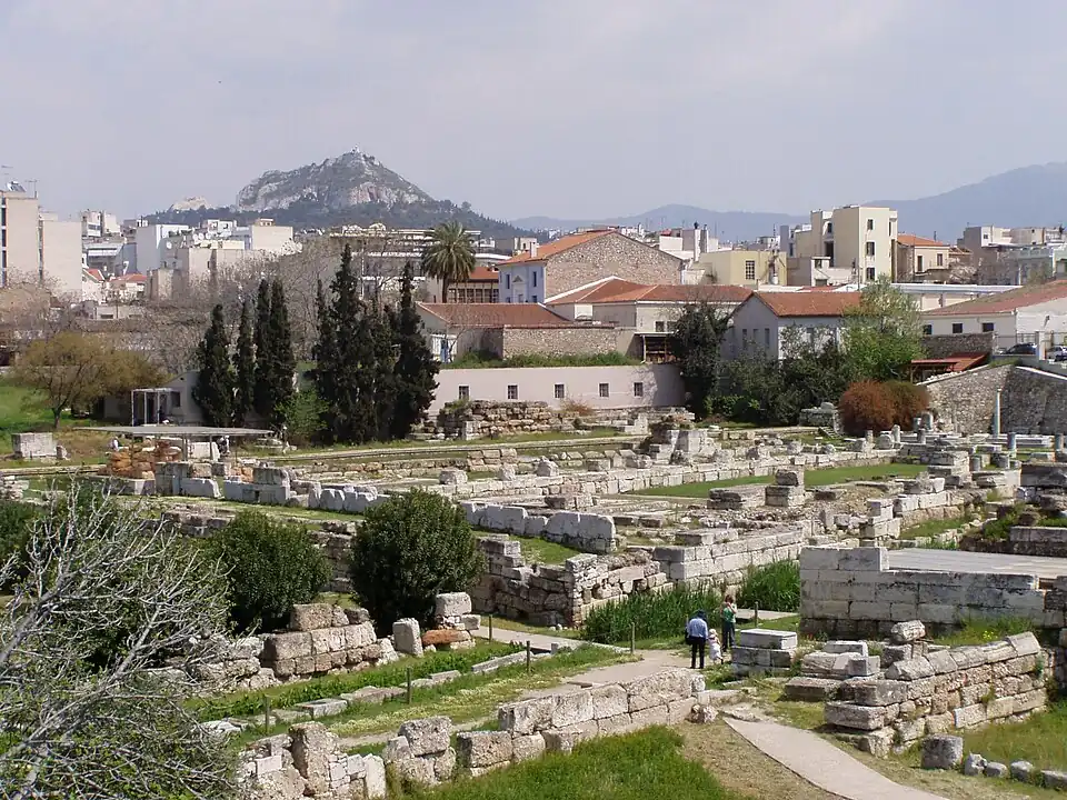 Vista desde fuera de la muralla de Atenas. Puerta y Vía sagrada (personas abajo derecha) con el Erídano. Dípilon (arriba izquierda bajo techo). Año 2008.