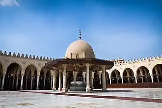 Photo of a paved courtyard surrounded by an arcade, with a domed pavilion in the centre over a well