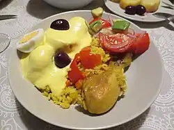 Arroz amarillo con pollo, acompañado de papa a la huancaína y ensalada de aguacate y tomate, en Perú