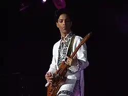 Prince tocando la guitarra con una camisa blanca con pedrería.