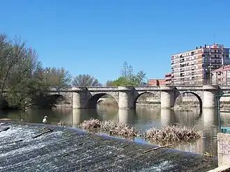 La foto muestra un puente de piedra con cinco arcos sobre el río.