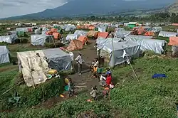 Kibumba es un campo de desplazados a unos cuarenta minutos al norte de Goma, cerca de la frontera con Ruanda. Está construido sobre las ruinas de los campos de refugiados ruandeses. La población proviene de Rugare, a unos 10 km de distancia, y de Tongo, a unos 40 km de distancia. Está gestionado por los propios desplazados y la ONU y ONG prestan servicios en el campo de acuerdo con el Comité de Desplazados. UNICEF, junto con ONG asociadas, está gestionando un área para que los niños jueguen y donde podamos escuchar cualquier problema que puedan tener los niños, estamos apoyando la educación de emergencia, puntos de agua, letrinas y apoyo psicosocial y médico para las sobrevivientes de violaciones.