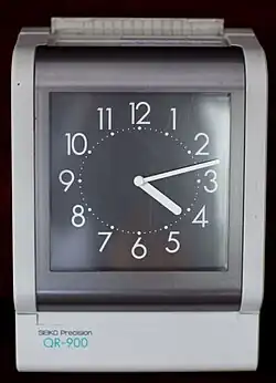 Reloj de fichar eléctrico sobre tarjeta de cartón.