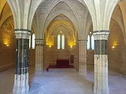Sala Capitular del Monasterio de Piedra. Presenta 4 columnas antes policromadas, ahora descoloradas, con restos de pintura azul; al fondo, una mesa roja. Toda la sala está rodeada por un banco continuo.