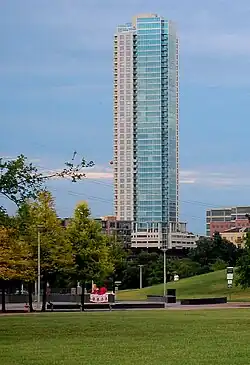 Ground view from the south of a 43-story tower. The building has a green glass facade on the right side, and a solid brick side with windows on the left.