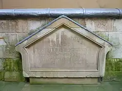 Una construcción triangular desgastada de piedra con una desgastada inscripción grabada.