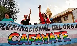 Mujeres trans y cis sostienen la bandera de arrastre del inicio de la movilización, están en frente de la catedral de Cafayate.