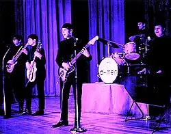 Una fotografía coloreada de los cinco miembros de The D-Men presentándose.