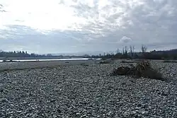 Photo shows a river bordered by an immense bed of white stones. There are mountains in the distance.