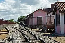 Imagem de um trilho de trem em primeiro plano e, à direita, edificação antiga de parede rosa com a estação e a inscrição Bebedouro em branco