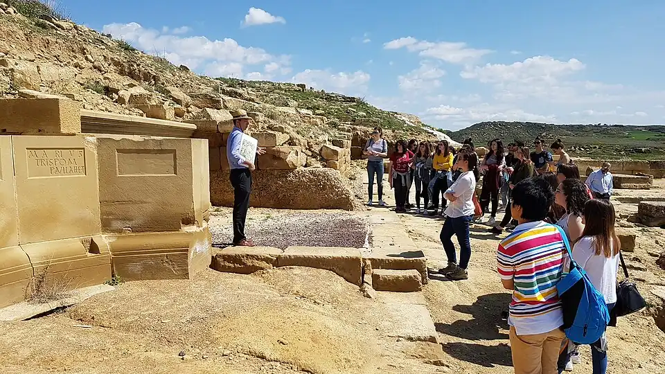 Javier Andreu explicando y mostrando a los visitantes del yacimiento romano de Los Bañales (Uncastillo) el contenido de los restos hallados (2018).