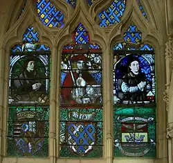 Vitral derecho de la capilla de santa Ana (tercera capilla lateral norte),, de Valentin Bousch (excepto parte derecha del siglo&nbsp;XIX). Los personajes son (de izda. a dcha.): : Fiacre Fériet, notable y comerciante, San Adrian, Jeannon Thiriet, esposa del primero. Por debajo, armas de Lorena, de dnjou y de la ville de Saint-Nicolas.